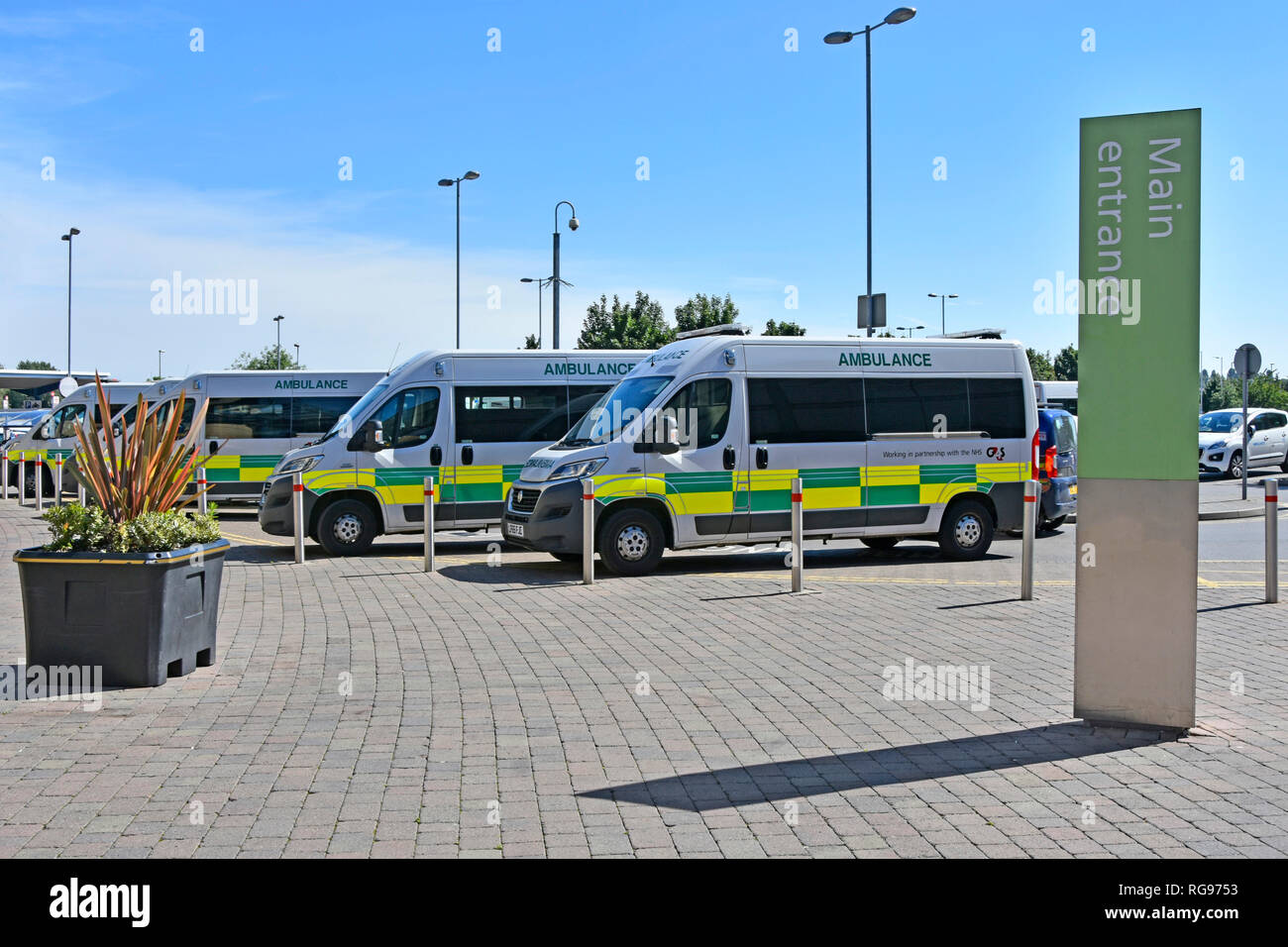 Fila di G4S di somministrazione al paziente ambulanza sanitaria parcheggiata fuori l'ingresso principale segno di NHS Queens Hospital Romford Havering Est Londra Inghilterra REGNO UNITO Foto Stock