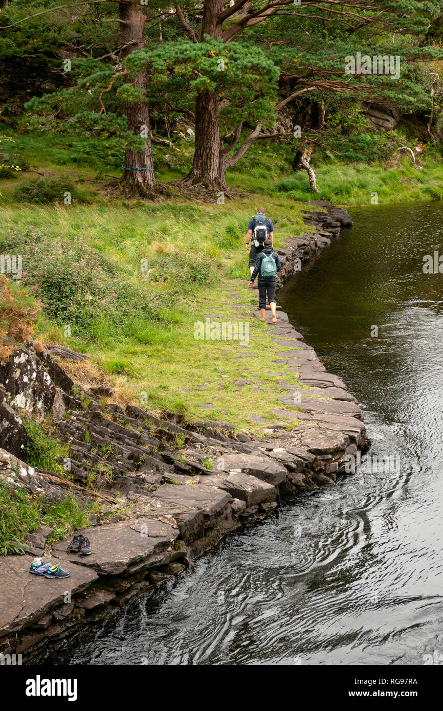 Escursionismo in Irlanda. Due backpackers giovane turisti camminare a piedi scalzi lungo il fiume di montagna stream. Parco Nazionale di Killarney, Co. Kerry, Irlanda. Foto Stock