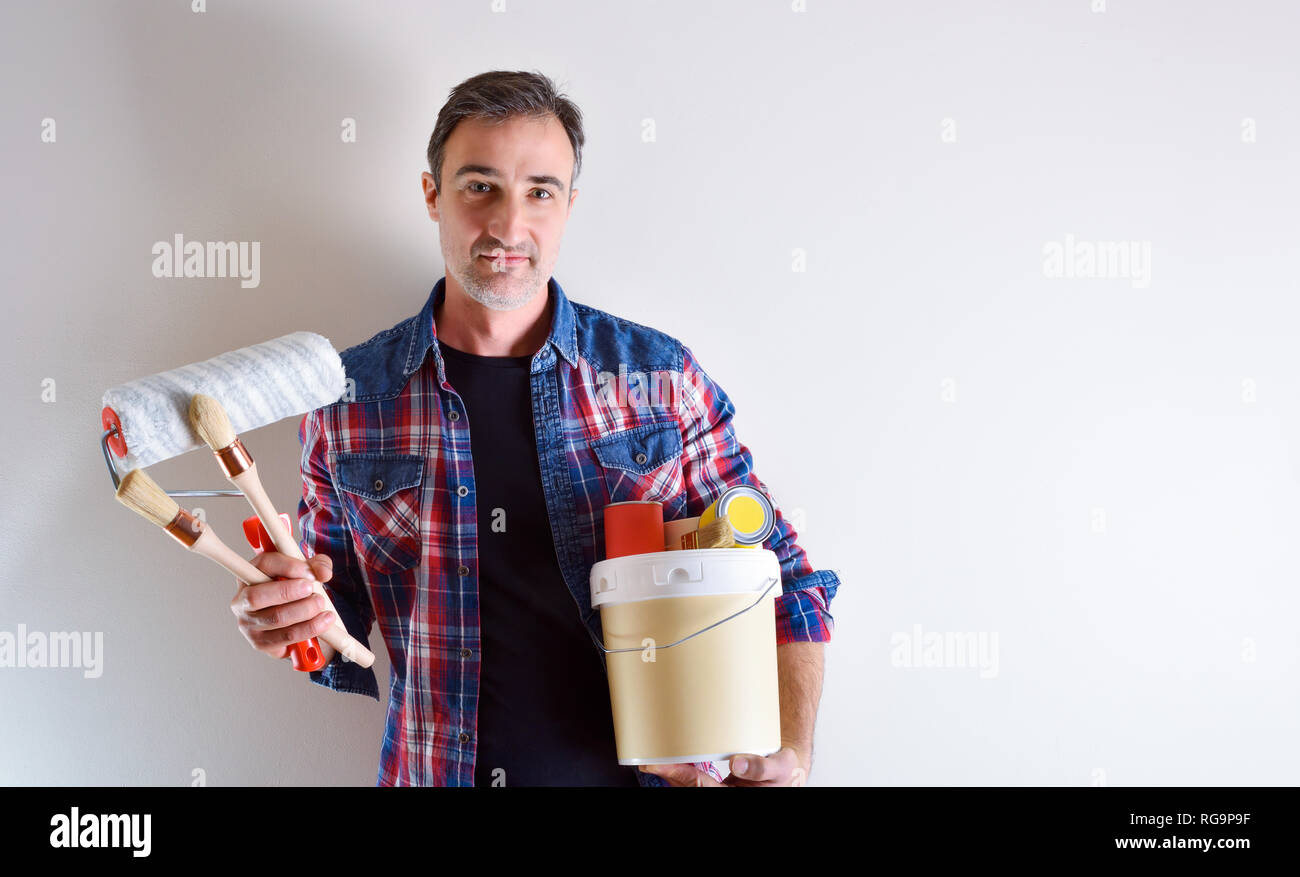 Uomo con strumenti di vernice su mani e muro bianco dietro. Home Diy concetto. Vista frontale. Composizione orizzontale. Foto Stock