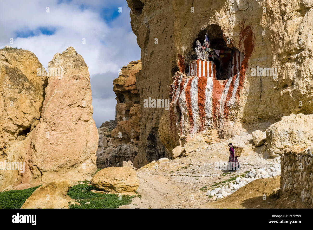 Un rosso e bianco buddista dipinto grotta santuario situato in una scogliera di roccia, una donna locale con un cestello a piedi al di sotto di esso Foto Stock