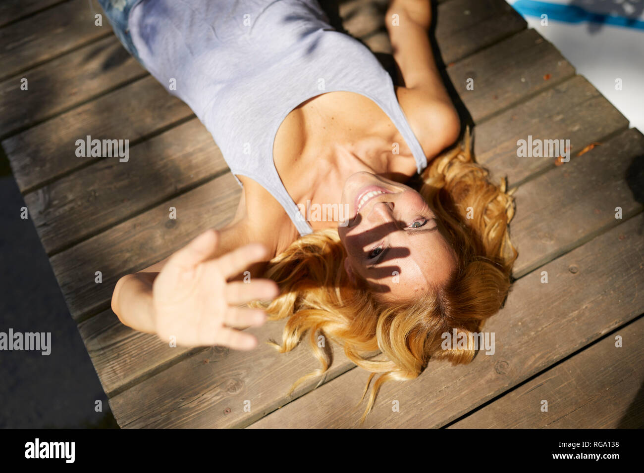 Felice donna bionda giacente sul pontile in legno nella luce del sole Foto Stock