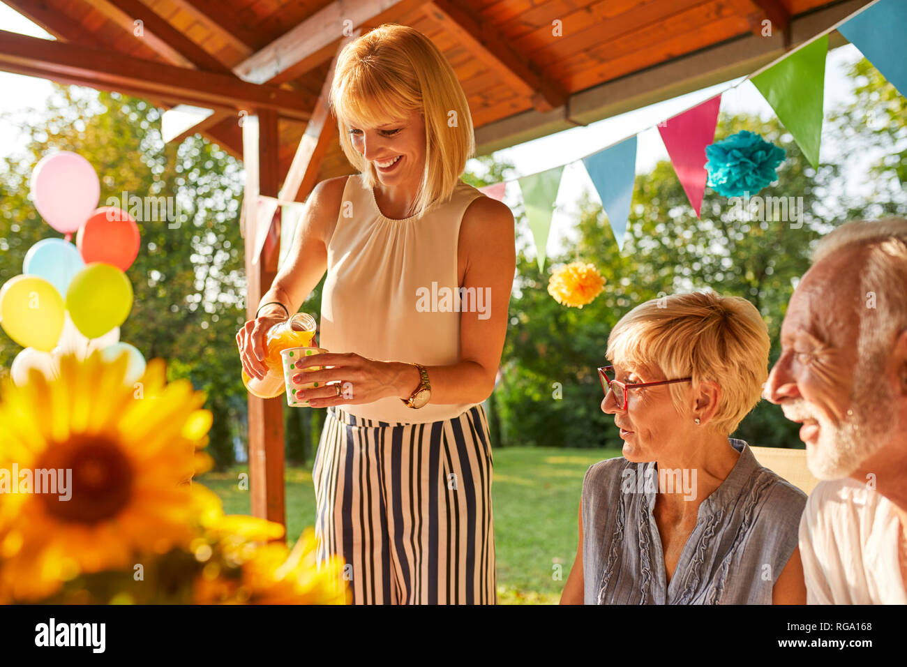 Donna felice che serve succhi di frutta su un party in giardino Foto Stock