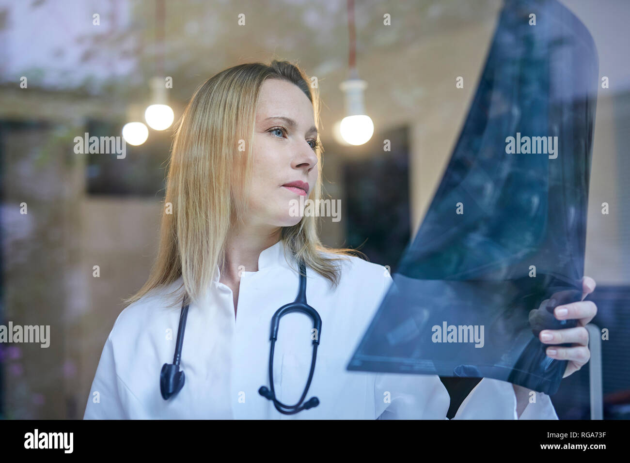 Medico donna guardando immagine a raggi x dietro il vetro di finestra Foto Stock