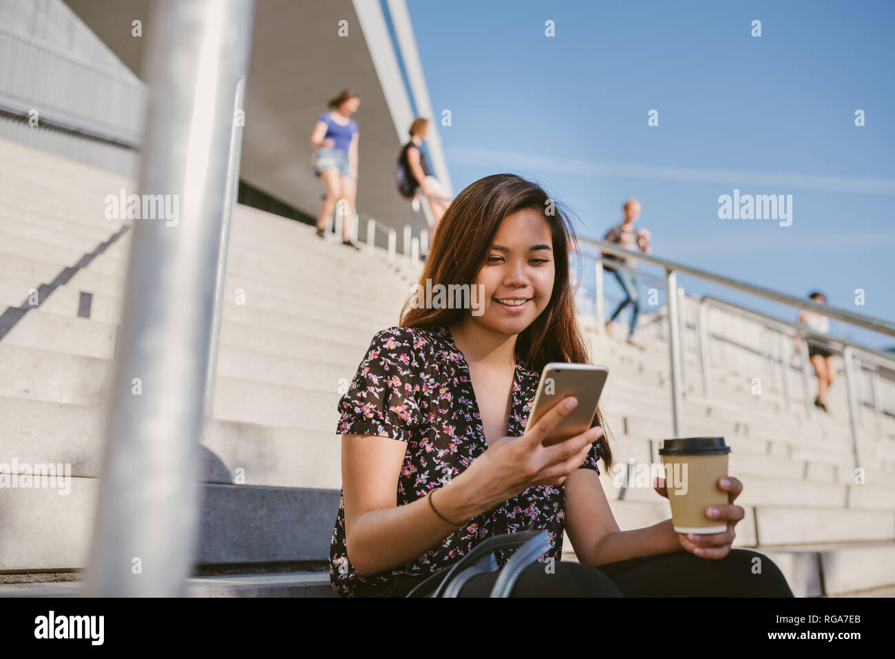 Sorridente Asian studente seduto sul campus di lettura di un messaggio al cellulare Foto Stock