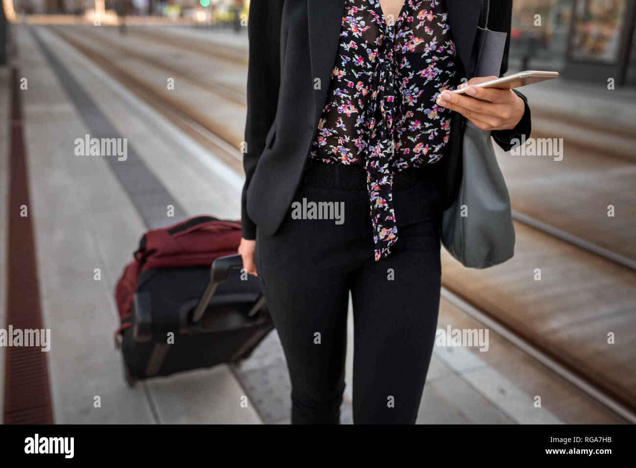 Primo piano di una imprenditrice a piedi con i suoi bagagli da una fermata del tram controllo volte con il suo cellulare Foto Stock