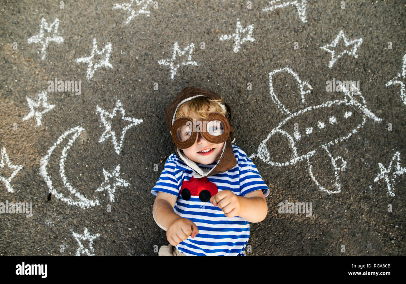 Ritratto di sorriso toddler pilota che indossa un cappello e occhiali giacente su asfalto verniciato con aereo, luna e stelle Foto Stock