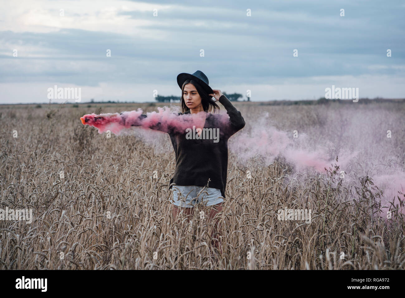 Ritratto di giovane donna in piedi in un campo di mais con torcia di fumo Foto Stock