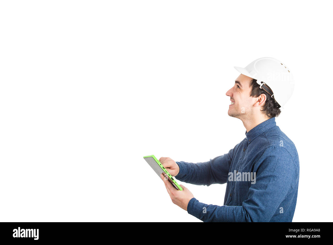 Vista laterale di allegro giovane ingegnere indossare casco protettivo utilizzando un computer tablet gadget guardando in alto isolato su sfondo bianco con copia Foto Stock