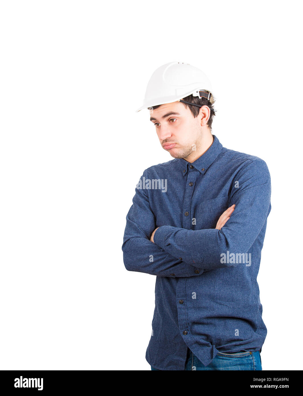 Stanco giovane ingegnere indossare casco protettivo tenendo le braccia incrociate guardando giù annoiato isolate su sfondo bianco con copia spazio. Foto Stock