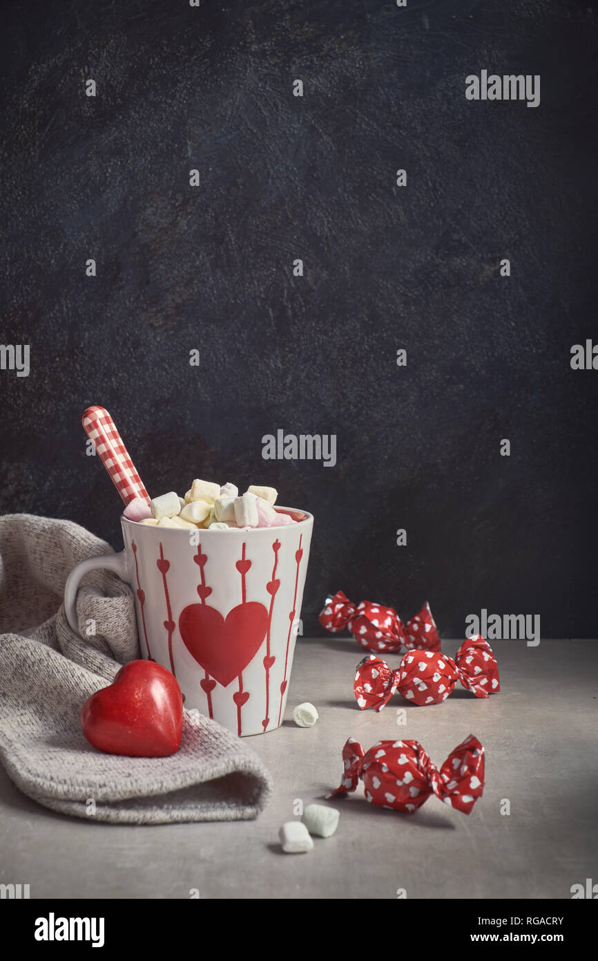 Cioccolata calda con marshmallows, cuore rosso sulla tazza, avvolto la caramella sul tavolo. Il giorno di San Valentino lo sfondo con il testo di saluto. Foto Stock