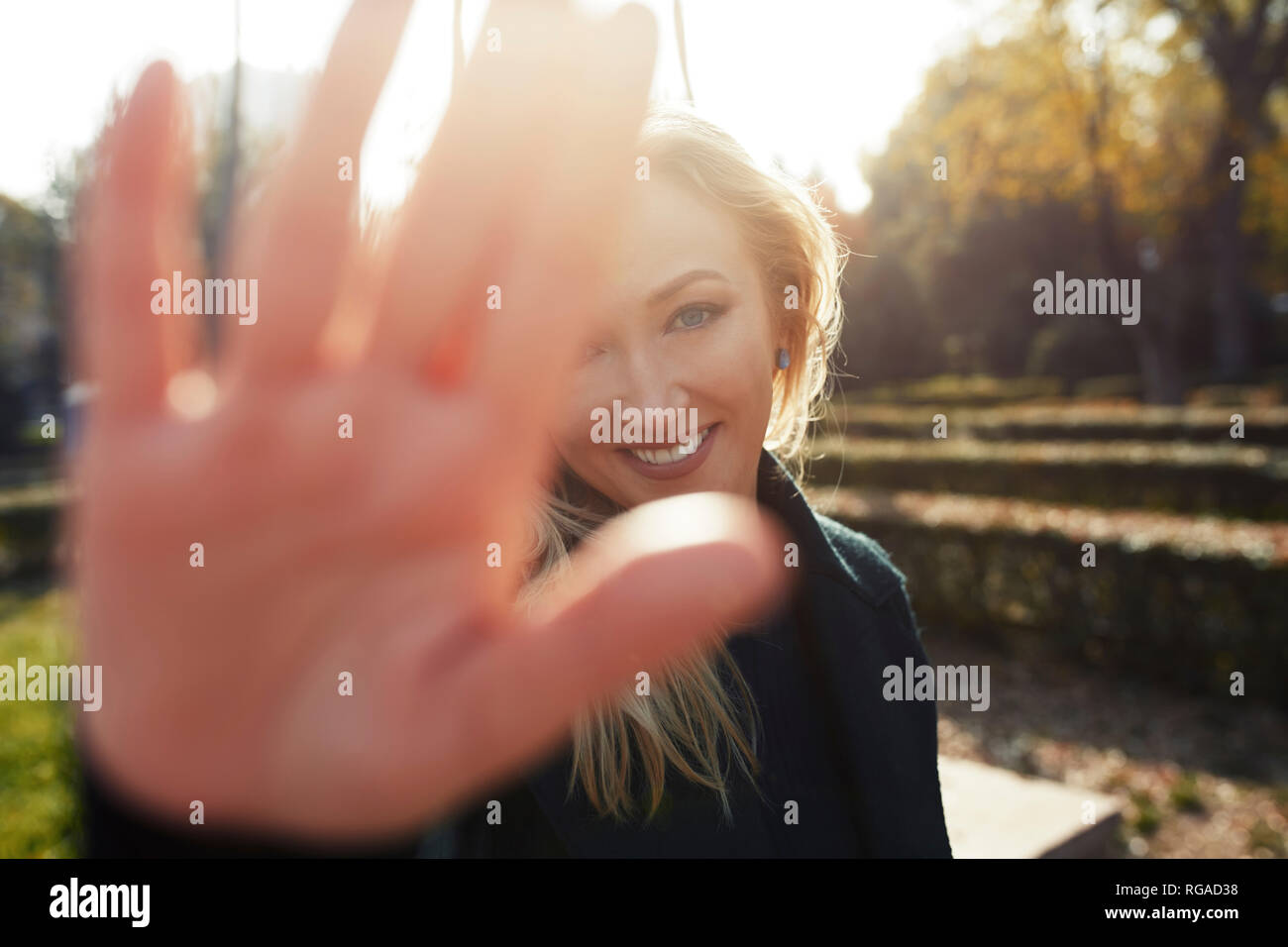 Ritratto di sorridere donna bionda alzando la mano in un parco Foto Stock
