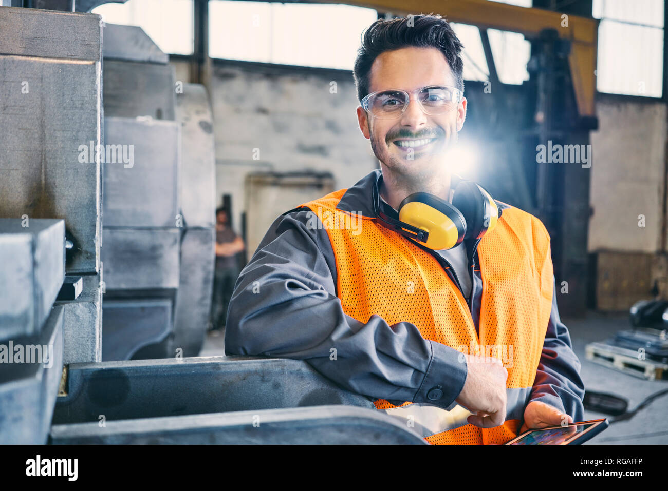 Ritratto di uomo sorridente indossando indumenti da lavoro protettiva e tenendo compressa in fabbrica Foto Stock