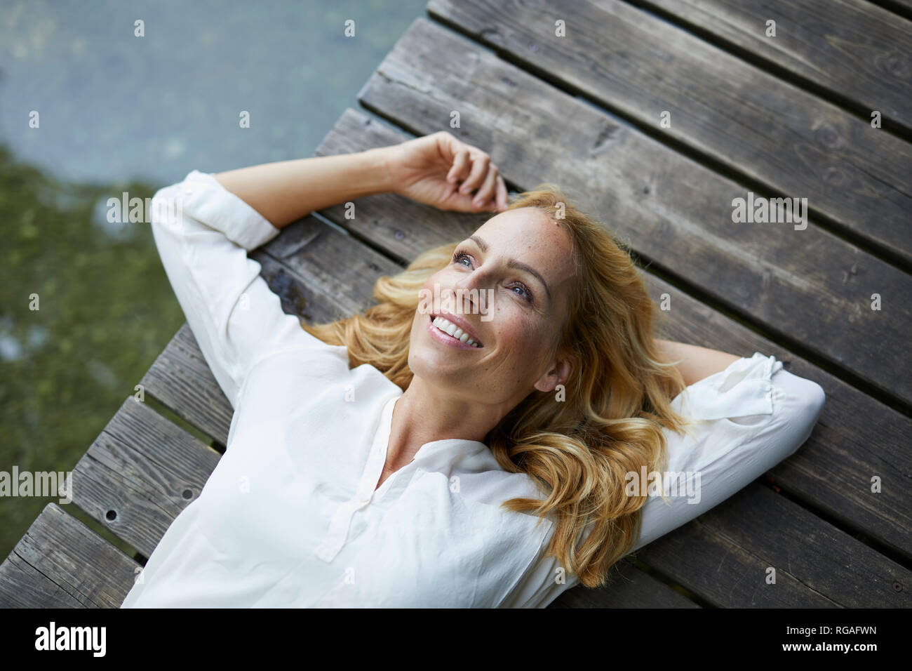 Sorridente donna bionda giacente sul molo di legno in un lago Foto Stock