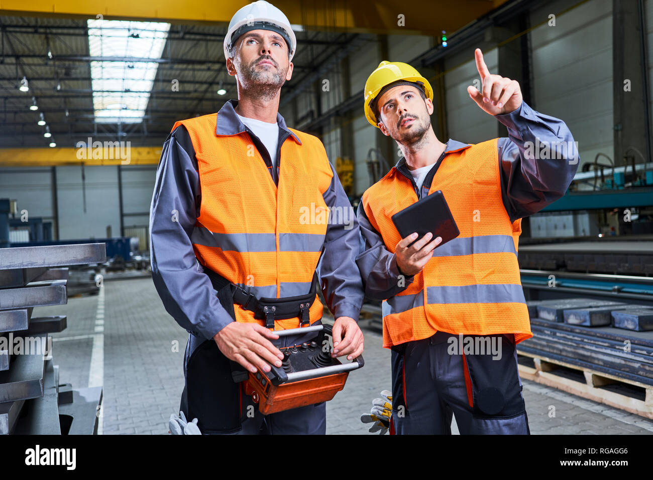 Due uomini in fabbrica parlando e funzionamento di macchinari con la console remota Foto Stock
