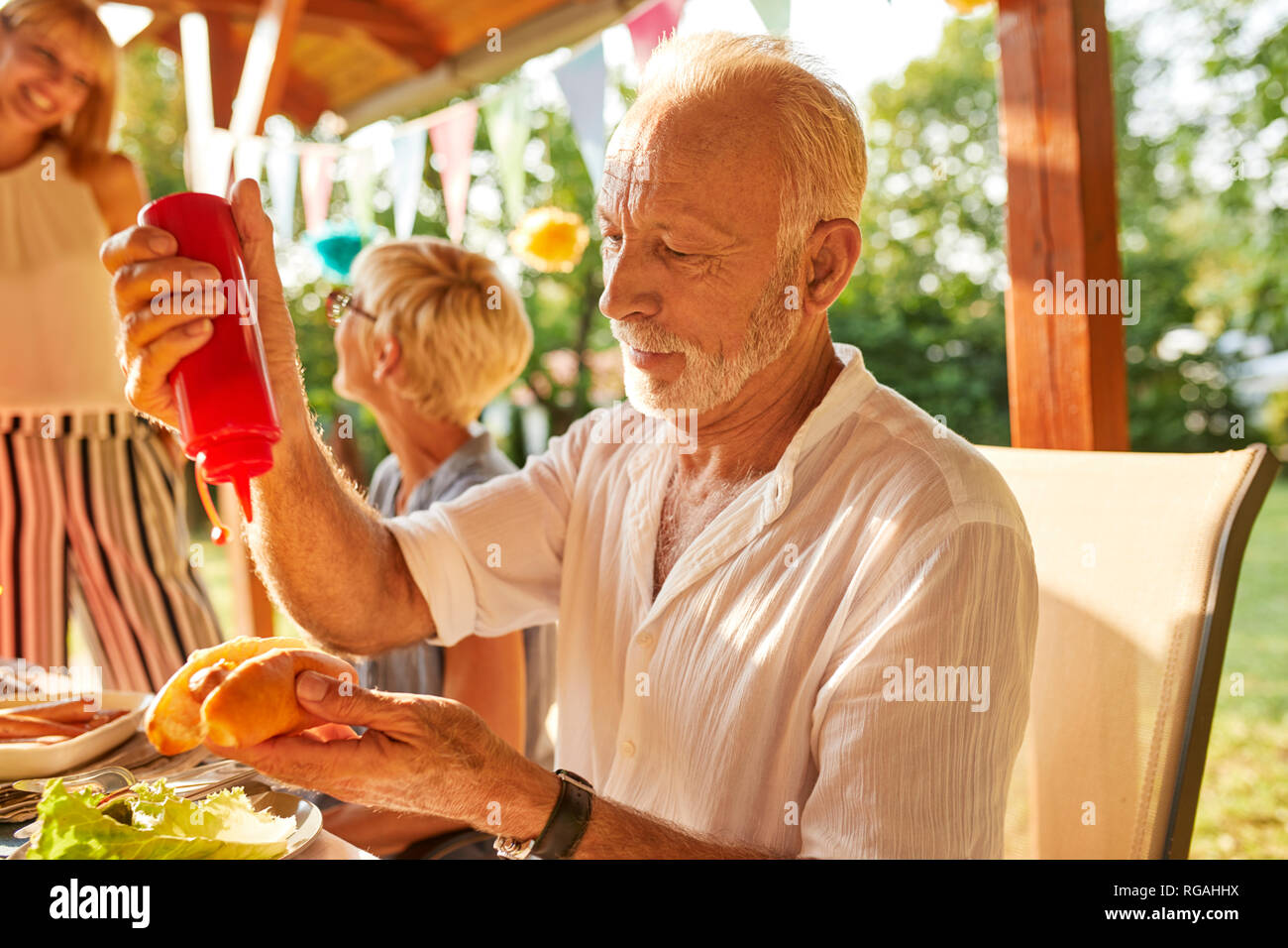 Senior uomo preparare un hot dog su un party in giardino Foto Stock