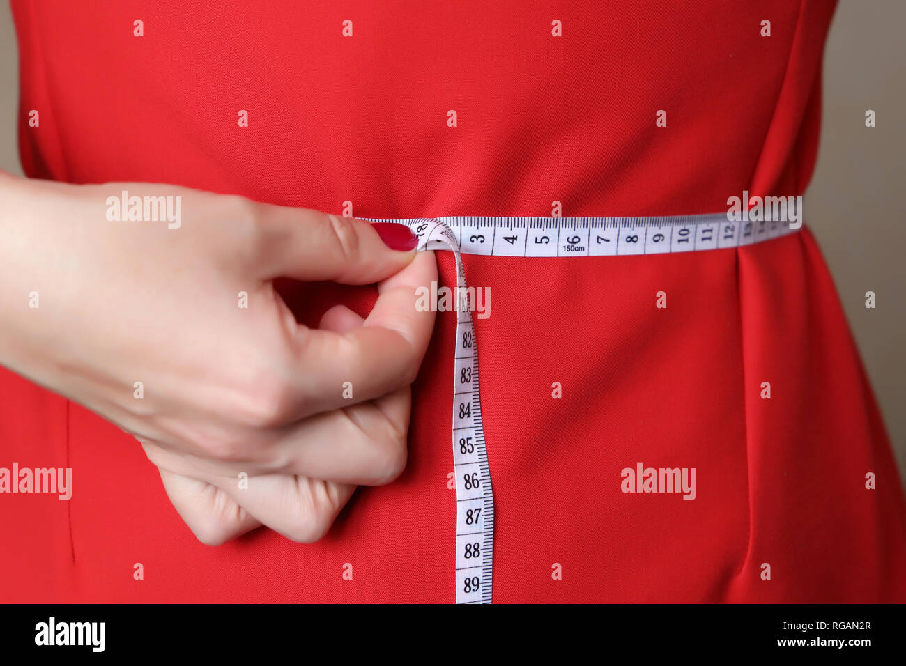 Ragazza in abito rosso con nastro di misurazione intorno alla vita. La perdita di peso, dimagrimento, dieta concetto, cura del corpo, vestiti di montaggio Foto Stock