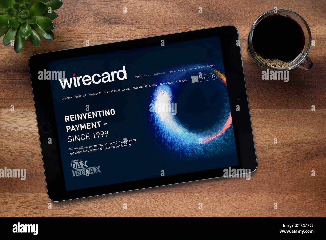 Il sito web di Wirecard è visto su un tablet iPad, su di un tavolo di legno lungo con un caffè espresso e una pianta di casa (solo uso editoriale). Foto Stock