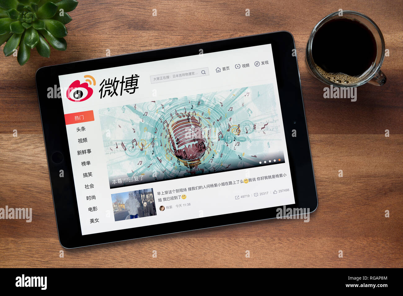 Il sito web di Weibo è visto su un tablet iPad, su di un tavolo di legno lungo con un caffè espresso e una pianta di casa (solo uso editoriale). Foto Stock