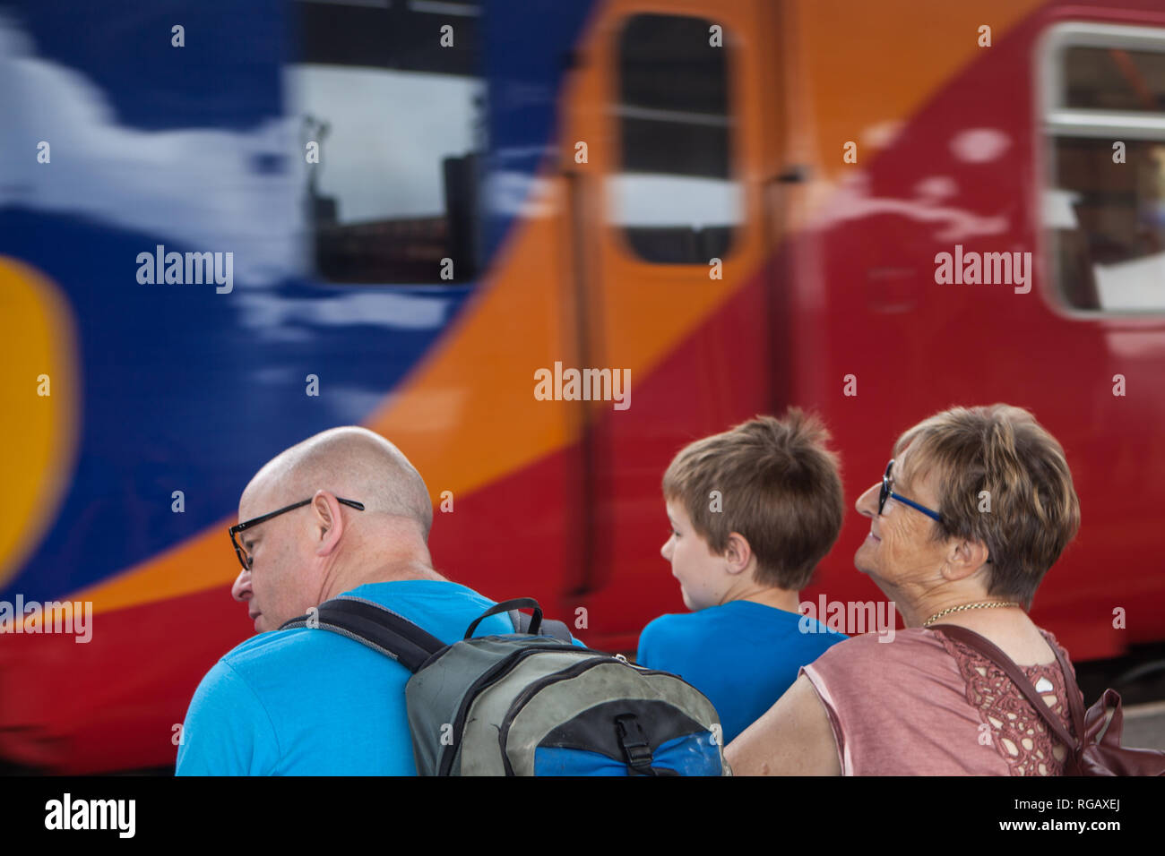 Famiglia caucasion seduto su una banchina della stazione con il treno in background in attesa di viaggiare. Foto Stock