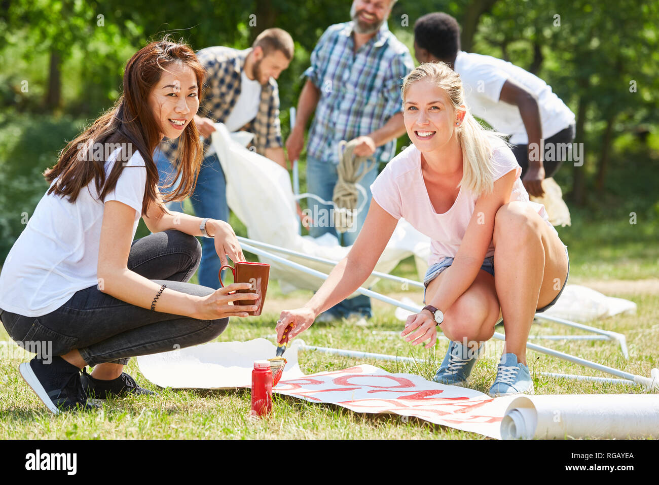 Due giovani donne volontariato attivisti dipingere un poster insieme nel parco Foto Stock