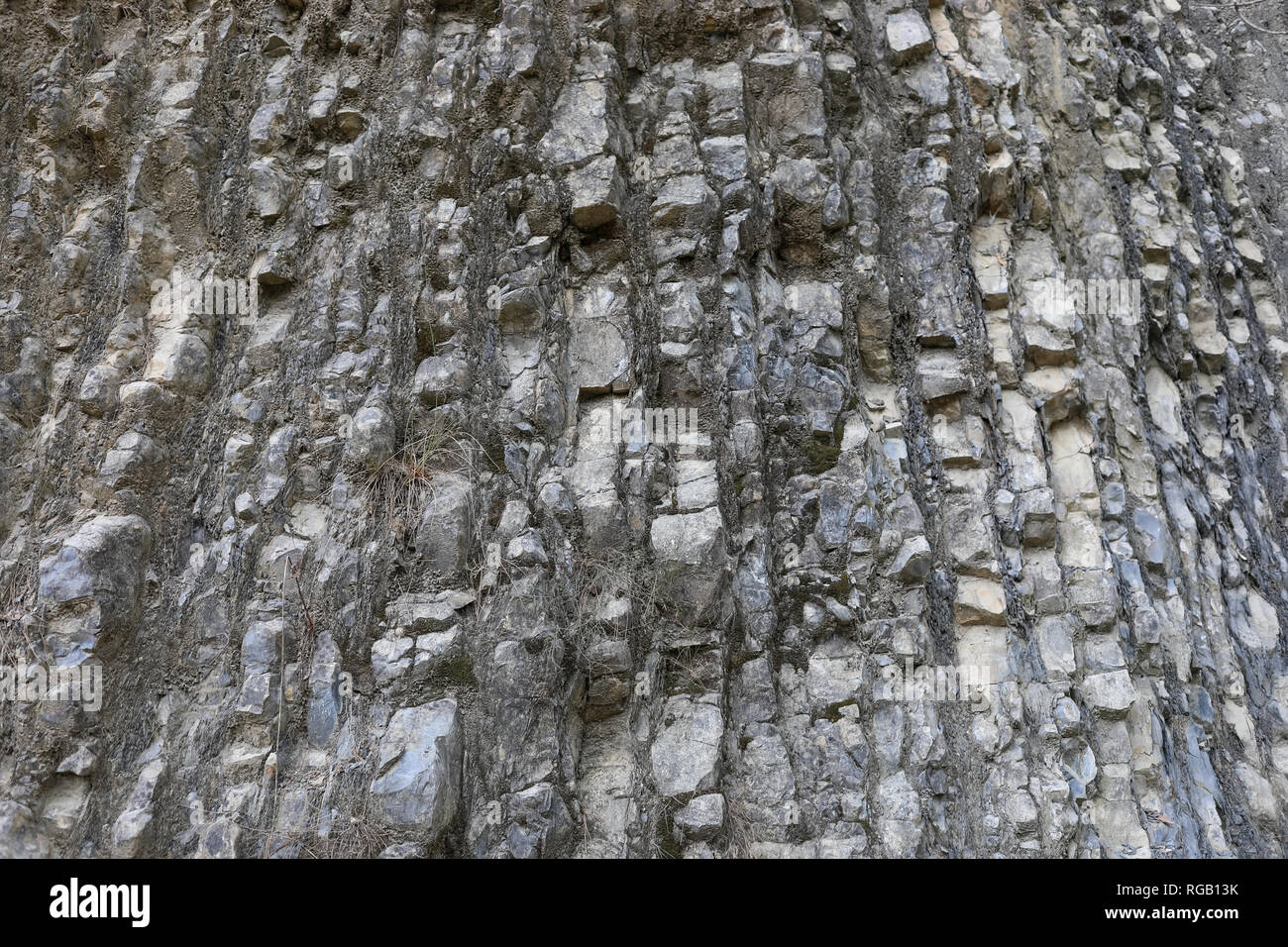 Naturale stratificato grigio pietroso parete di montagna con superficie irregolare come sfondo. Foto Stock