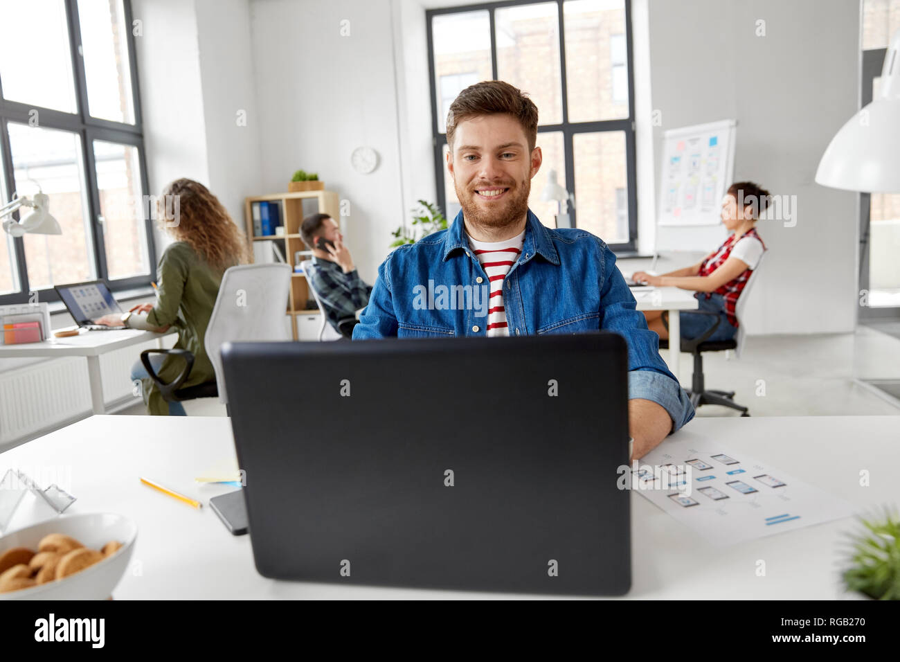 Sorridente uomo creativo con il computer portatile lavorando in ufficio Foto Stock