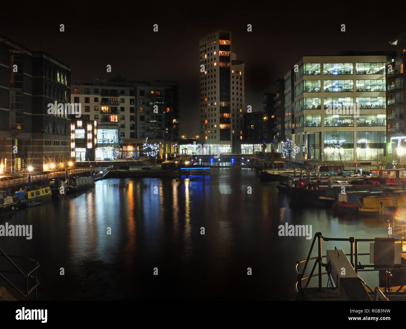 Clarence dock in leeds di notte con illuminato edifici riflessi nell'acqua e imbarcazioni ormeggiate lungo i lati Foto Stock