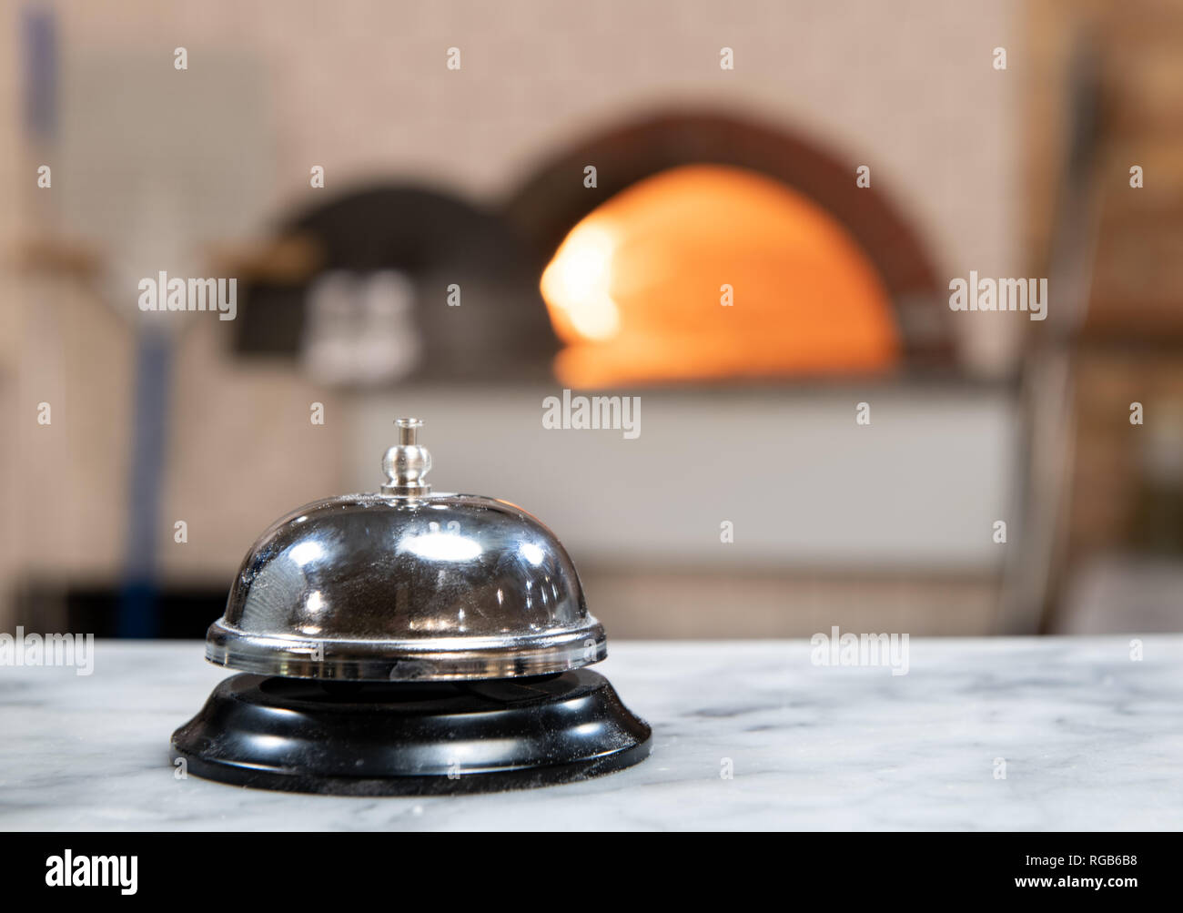 Close up della campana di servizio in pizzeria piano di lavoro, lo sfondo sfocato con forno a legna e Rosso fuoco Foto Stock