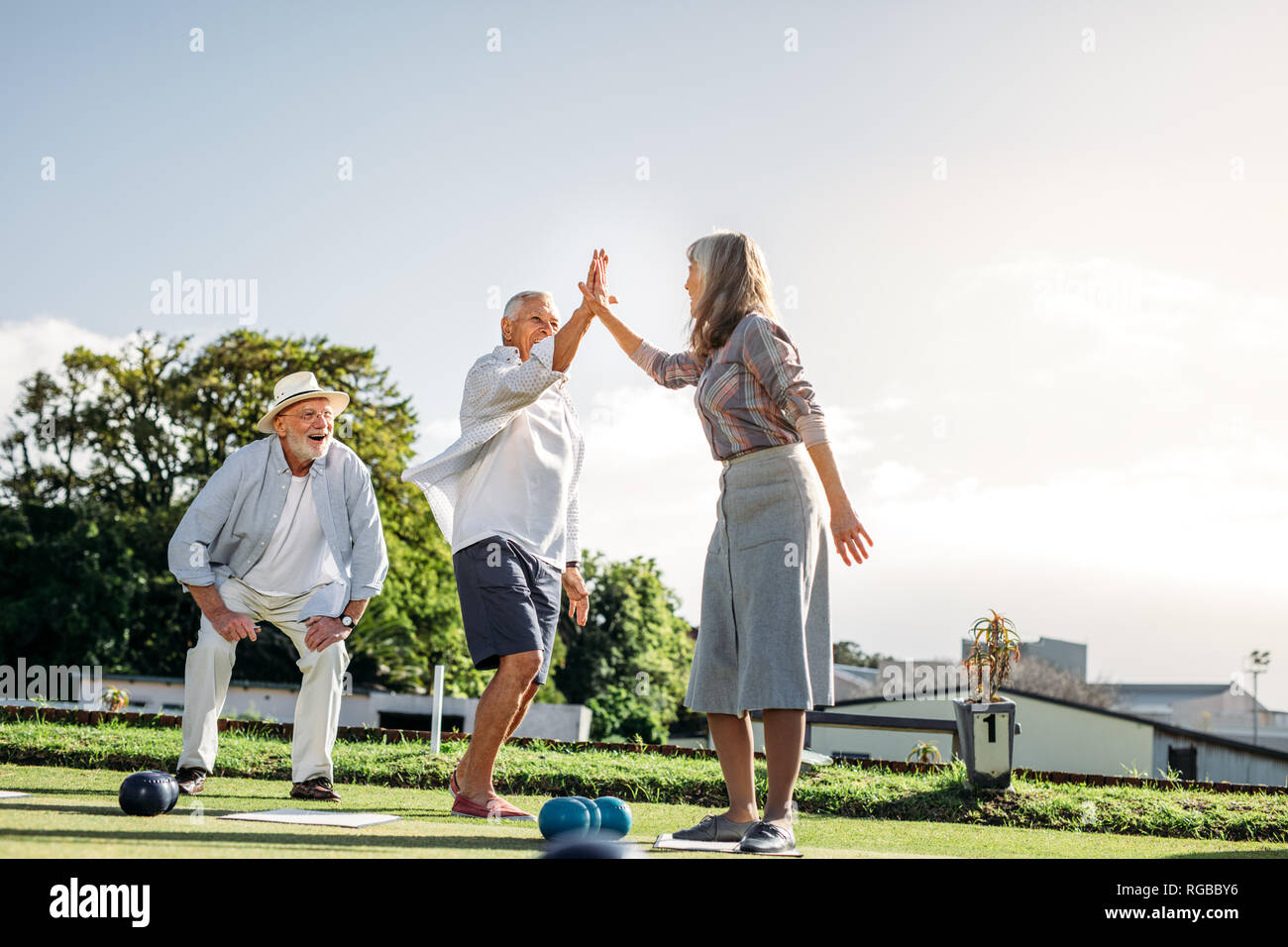 Senior l uomo e la donna dando alta cinque celebra il successo. Le persone anziane godendo di un gioco delle bocce in un parco. Foto Stock