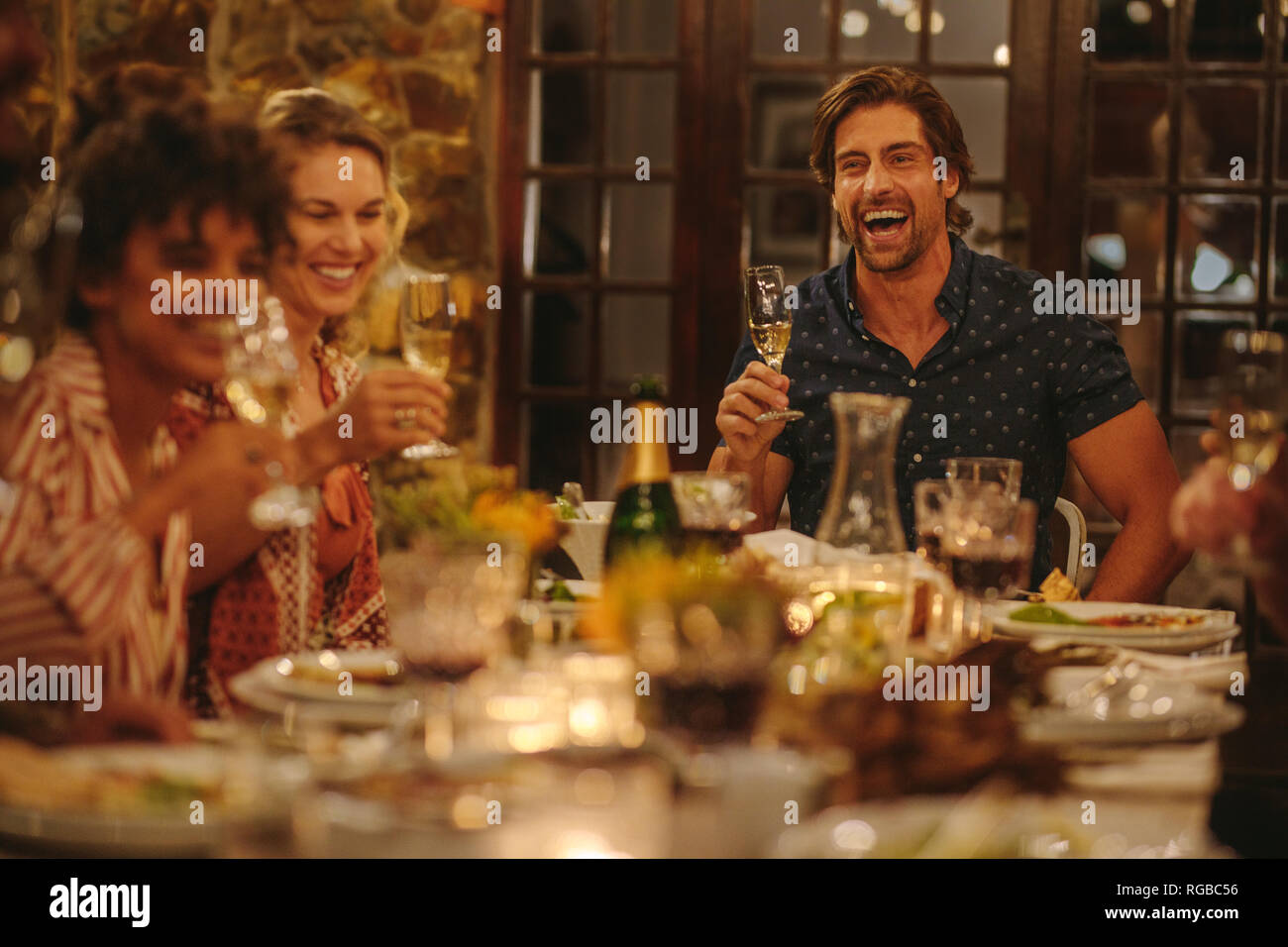 I giovani allegri avente le bevande a cena. Gruppo di amici seduti attorno ad un tavolo gustando cena con bevande. Foto Stock