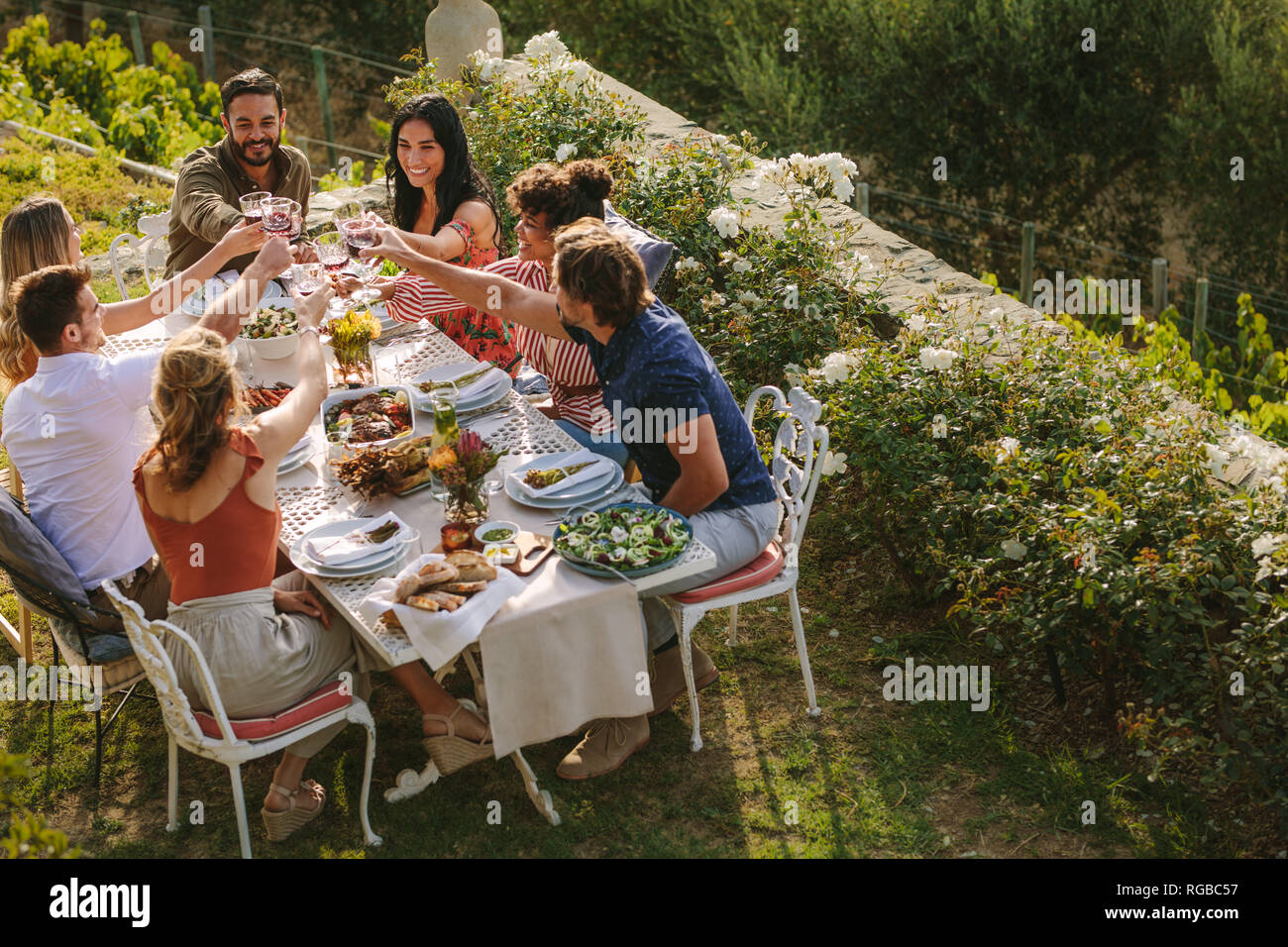 Un gruppo di uomini e donne seduti al tavolo e bevande di tostatura. Gruppo di amici Come tostare il vino a cena. Foto Stock