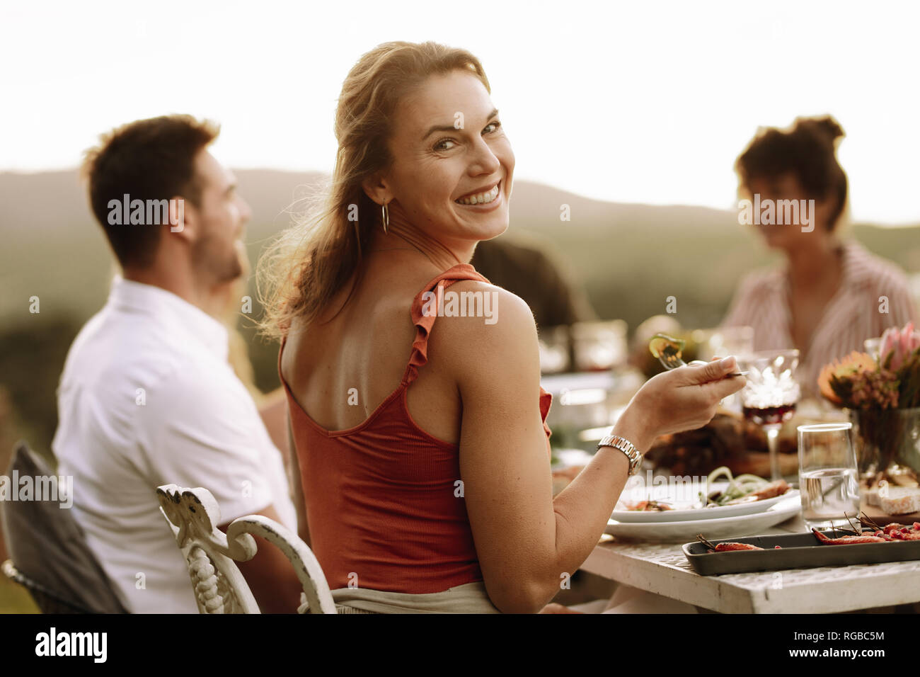 Bella donna avente il cibo con gli amici seduti a cena. La donna a mangiare cibo al party all'aperto con gli amici. Foto Stock