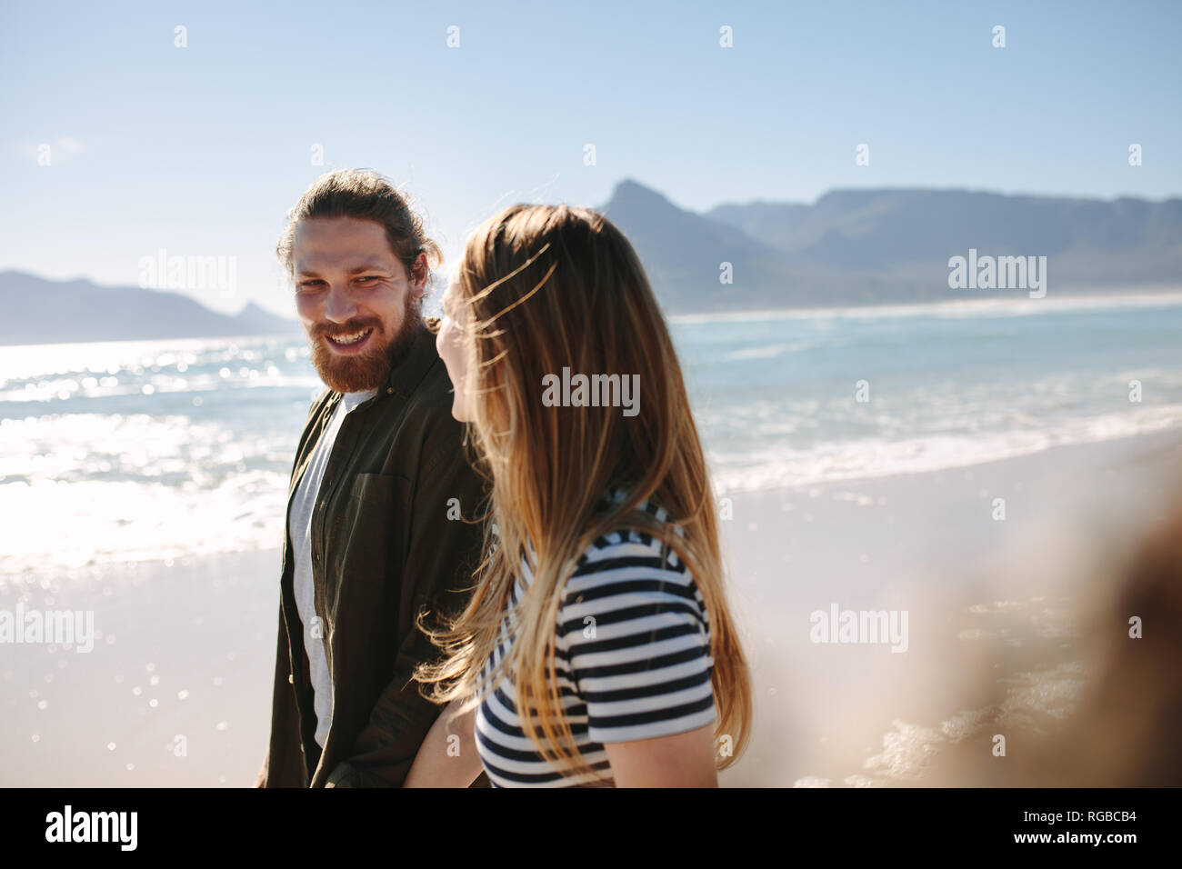 Bel giovane guardando la sua ragazza mentre passeggiate lungo la spiaggia. Coppia felice passeggiando all'aperto sulla spiaggia. Foto Stock