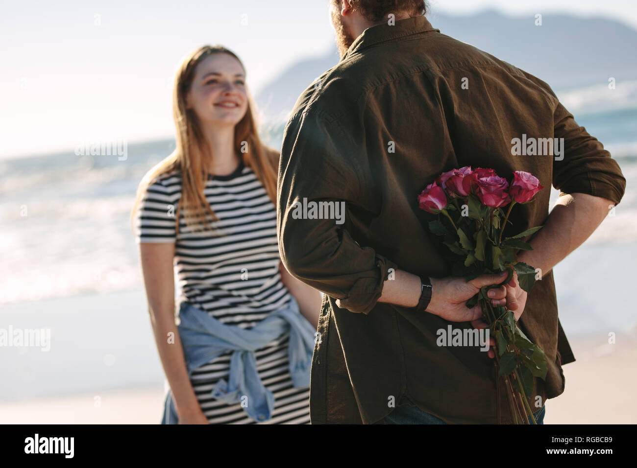 Coppia giovane in amore romantico data. Uomo con sorpresa mazzo di rose per la bella giovane donna sulla spiaggia. Foto Stock