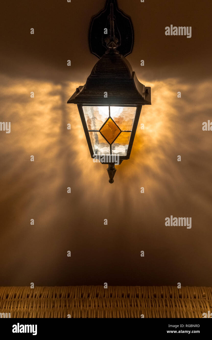 Vecchia lanterna in vetro arancione sul muro intonacato con ombre nel buio Foto Stock