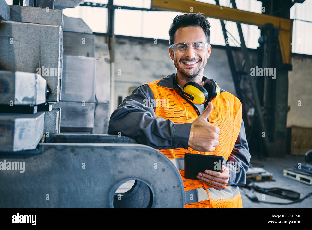Ritratto di uomo sorridente indossando indumenti da lavoro protettiva che mostra i pollici in su in fabbrica Foto Stock