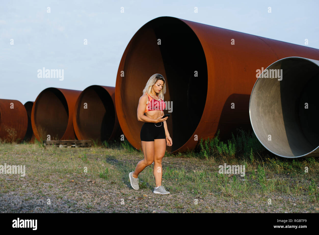 Athletic donna con un telefono cellulare e auricolari a piedi di sito industriale Foto Stock