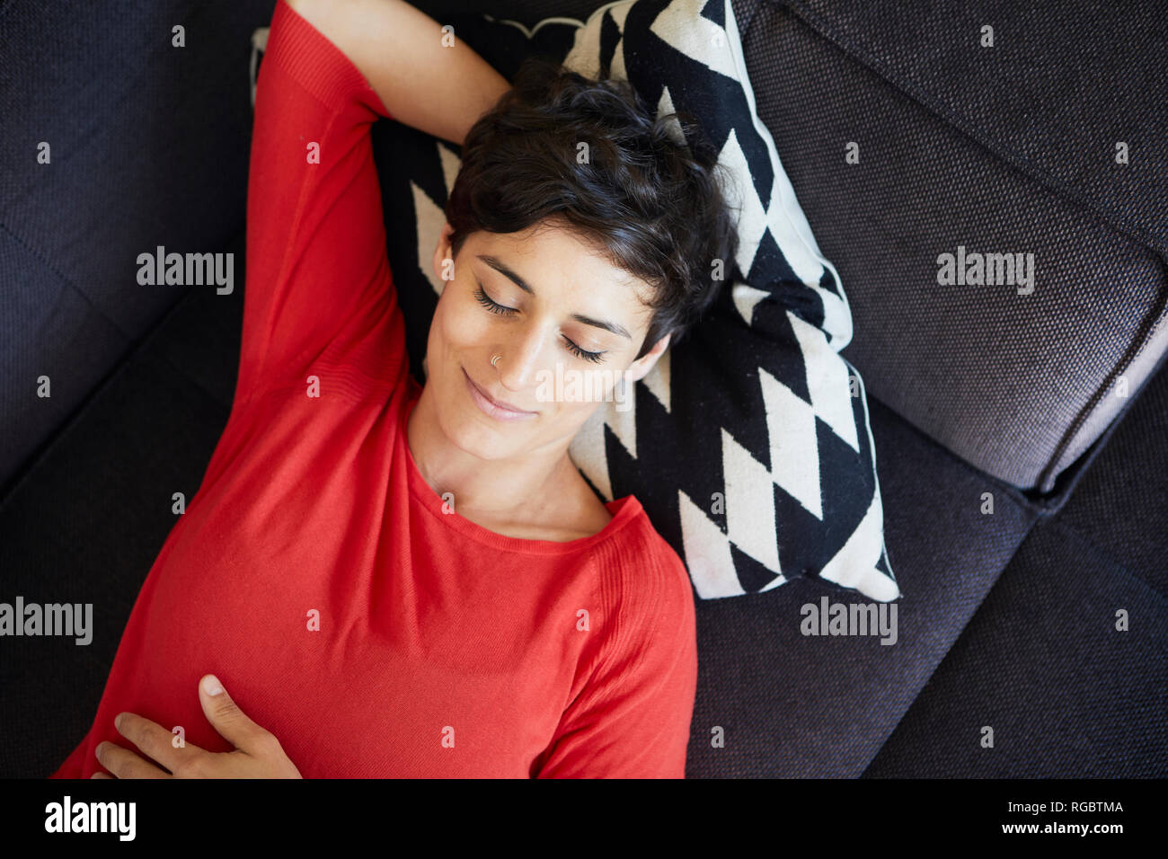Donna sorridente sdraiato sul lettino a casa con gli occhi chiusi Foto Stock
