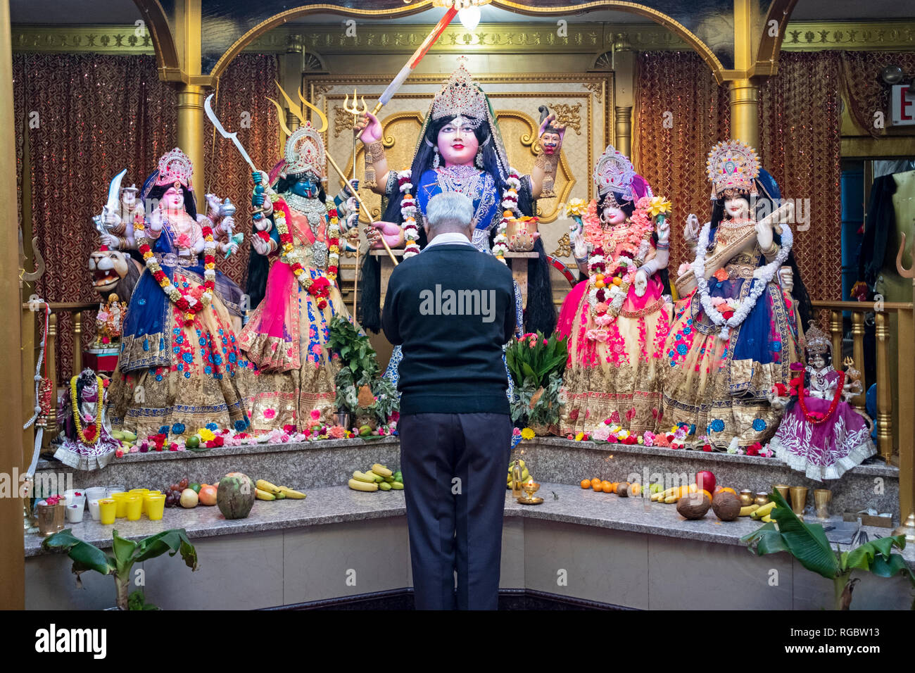 Un vecchio uomo con i capelli grigi gli archetti in silenziosa preghiera e meditazione se la parte anteriore di statue di divinità in un tempio indù nel Queens, a New York. Foto Stock