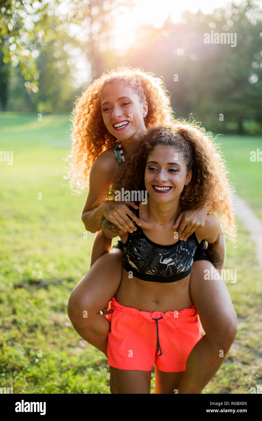 Ritratto di felice giovane donna dando il suo ridendo sorella gemella un piggyback ride Foto Stock