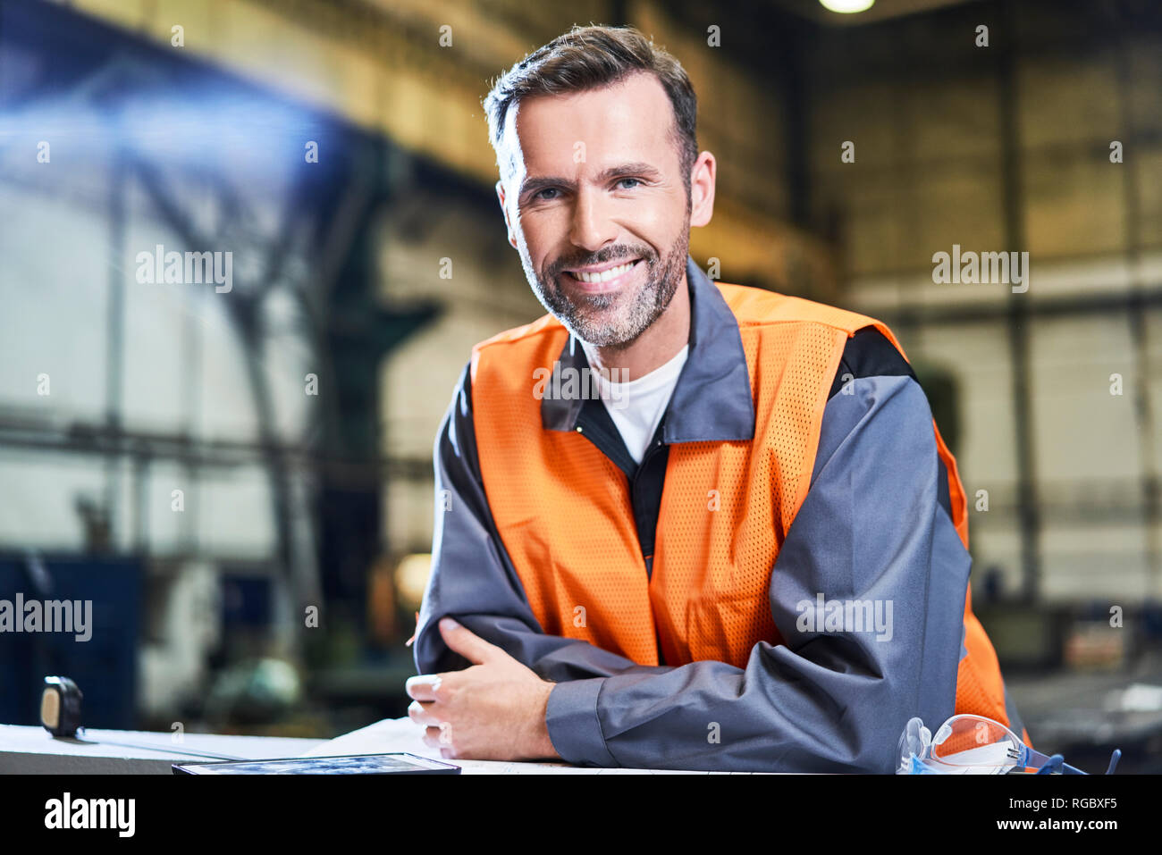 Ritratto di uomo sorridente in fabbrica indossando giubbotto di sicurezza Foto Stock