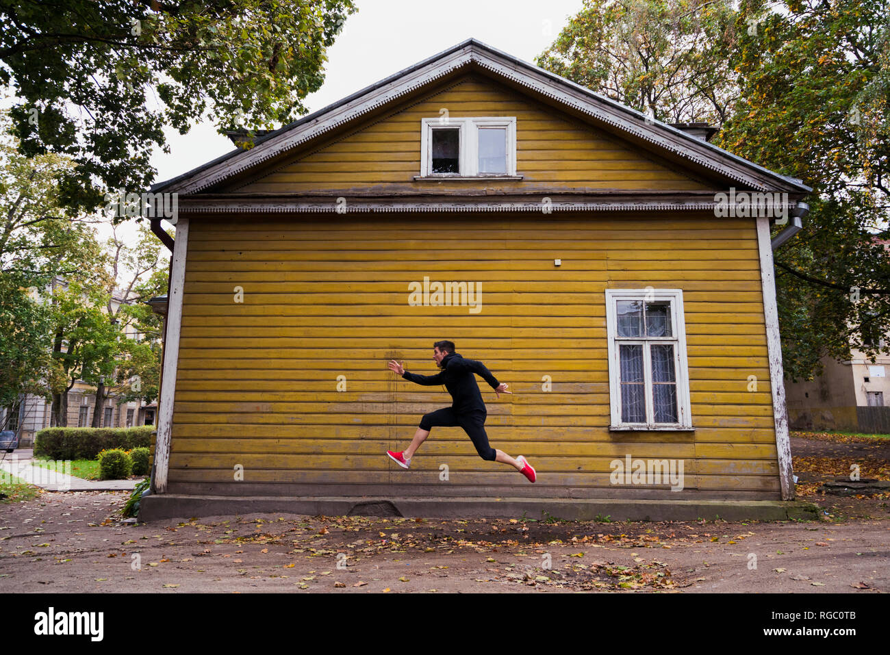 Dynamic atleta jumping nella parte anteriore di un giallo casa in legno Foto Stock