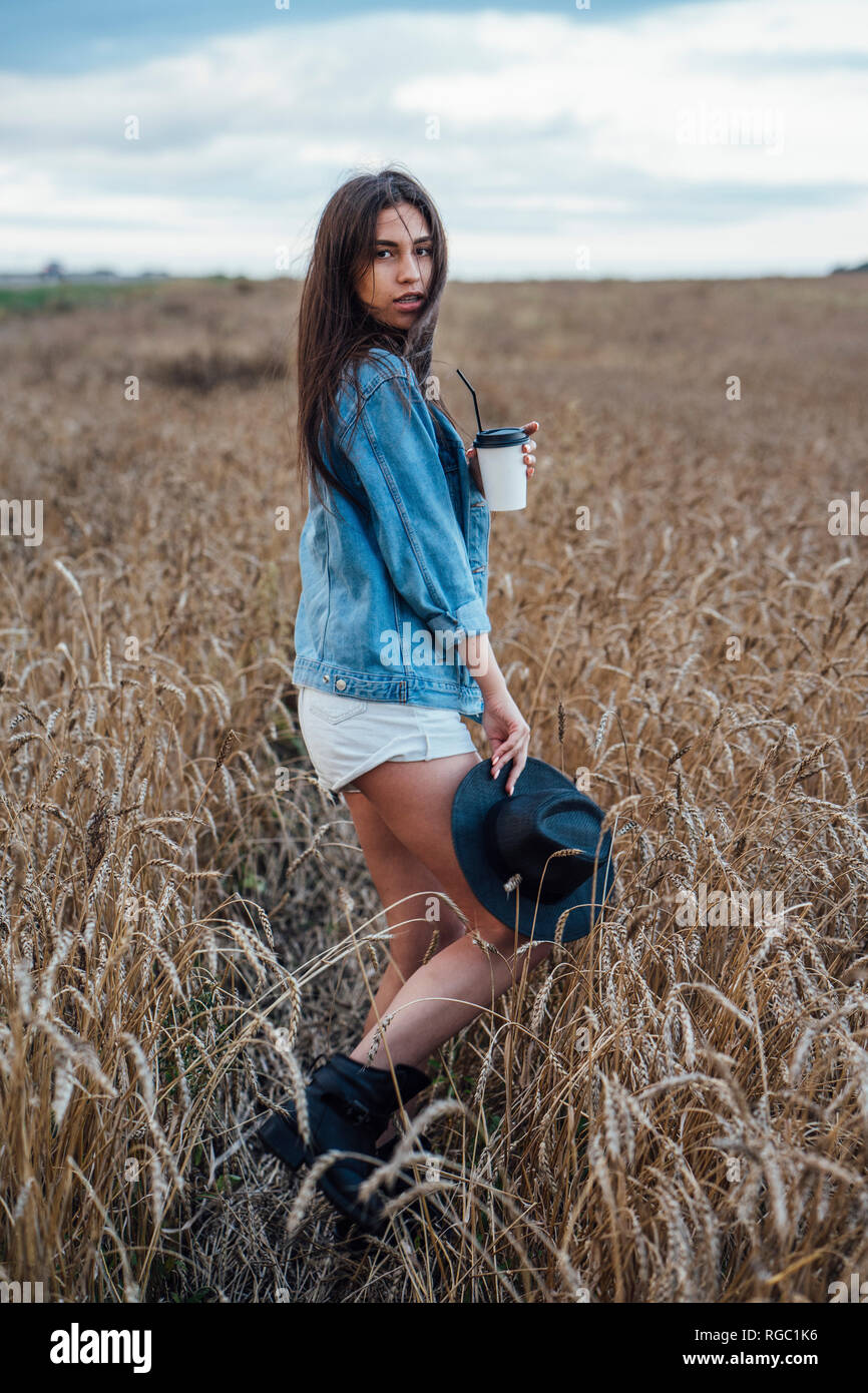 Ritratto di giovane donna con bevanda a piedi nel campo di grano Foto Stock