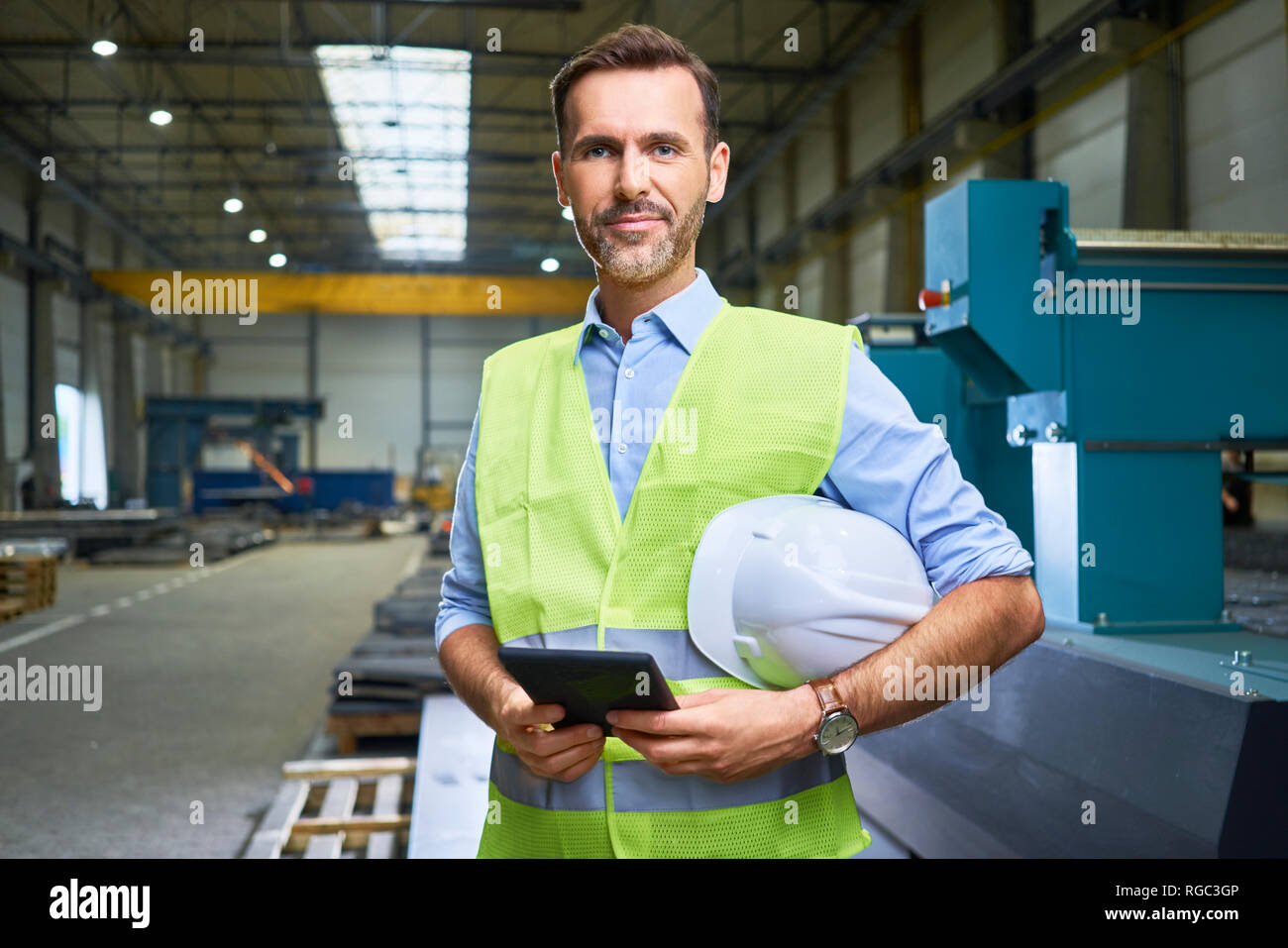 Ritratto di fiducioso uomo che indossa maglietta e giubbotto di sicurezza in fabbrica Foto Stock
