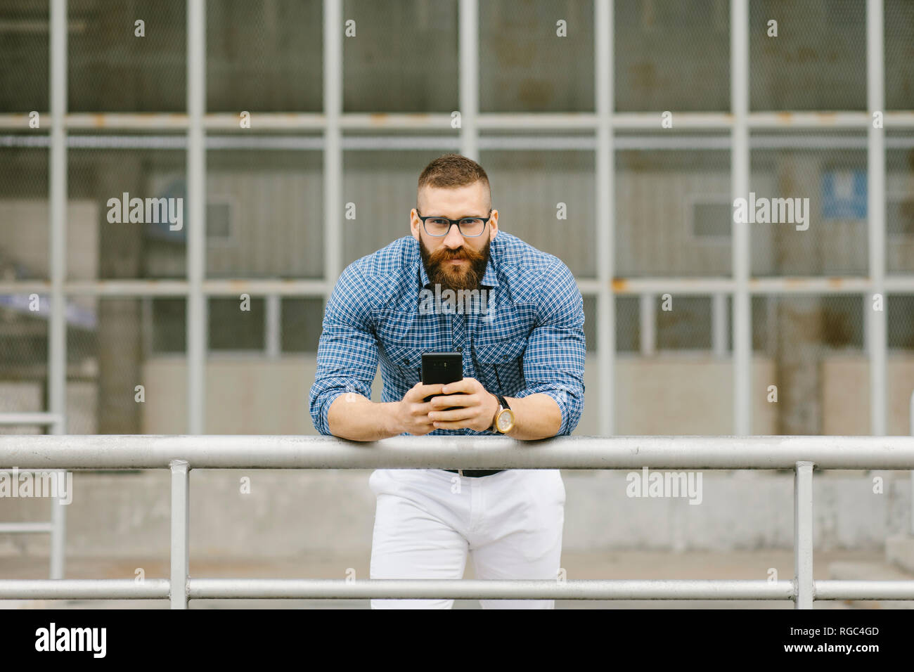 Ritratto di barbuto hipster imprenditore con inclinazione dello smartphone su parapetto Foto Stock