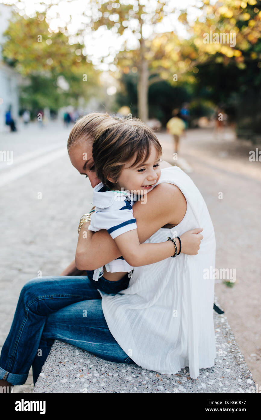 Madre seduta sul banco, cuddling con suo figlio Foto Stock