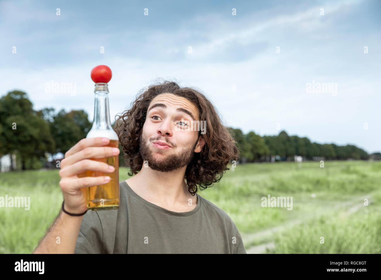 Ritratto di giovane sorridente uomo all'aperto di pomodoro di bilanciamento sulla bottiglia di birra Foto Stock