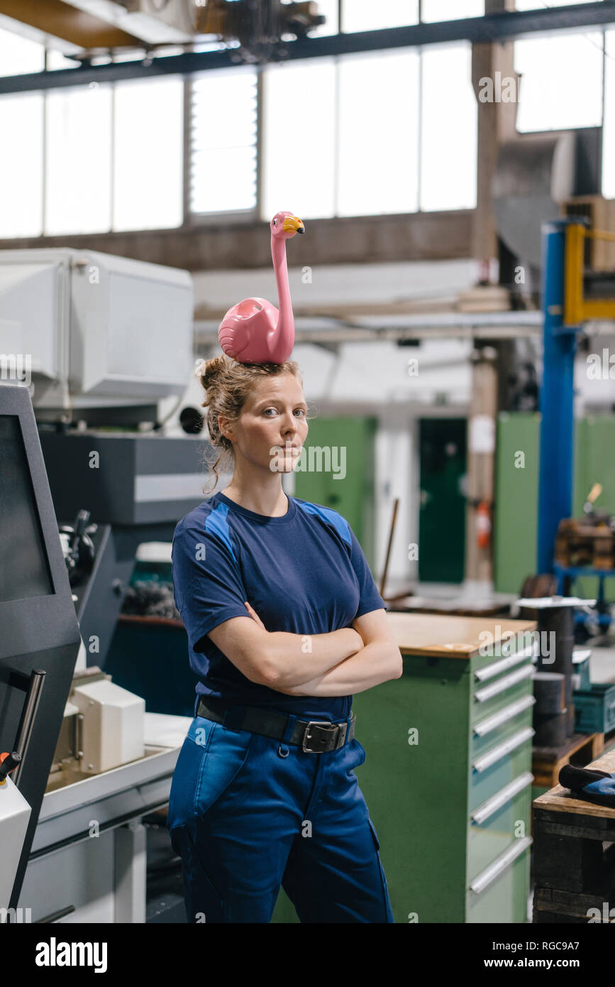 Giovane donna che lavora come un operaio specializzato in un high tech company, il bilanciamento di un fenicottero rosa sul suo capo Foto Stock