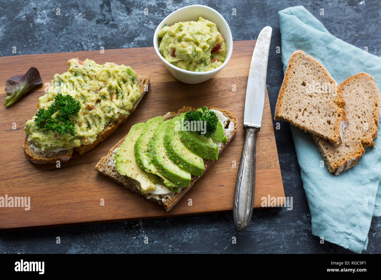 Fette di pane con fette di avocado e crema di avocado su pannello di legno Foto Stock