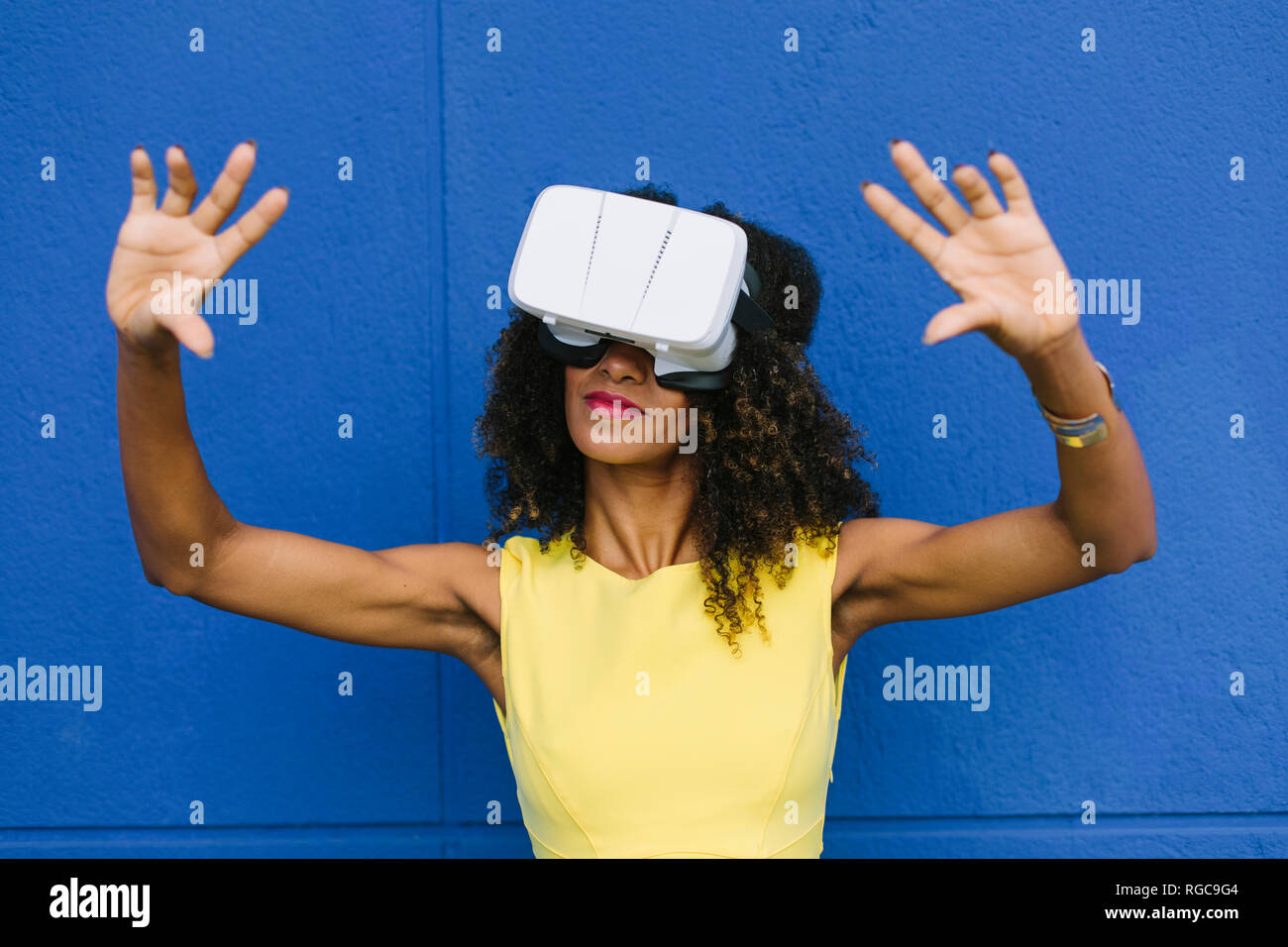 Donna che utilizza occhiali per realtà virtuale contro sfondo blu Foto Stock